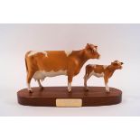 A Beswick model of a Guernsey cow and her calf, printed factory marks, on wooden plinth, 23cm wide,