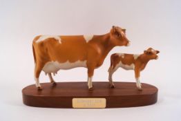 A Beswick model of a Guernsey cow and her calf, printed factory marks, on wooden plinth, 23cm wide,