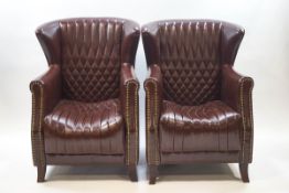 A pair of brown leather armchairs with brass studding and stitched detail,