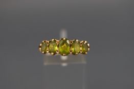 A hallmarked 9ct gold half hoop ring set with five graduated oval peridot. Scroll carved shoulders.