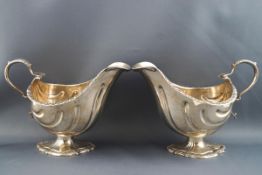 A pair of silver shell shaped sauce boats, each with double scroll handle and flared foot,