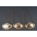 A pair of silver decanter labels embossed with shells and grapes, titled Whiskey and Gin,