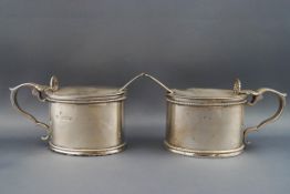 A pair of oval silver mustard pots, each with shell thumb piece and double scroll handles,