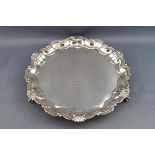 A silver salver, with cast shell and scroll border on three ball and claw feet,