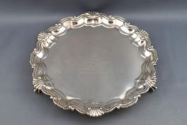 A silver salver, with cast shell and scroll border on three ball and claw feet,