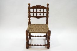 An oak child's chair with spindle back, turned and block supports, with a woven seat,
