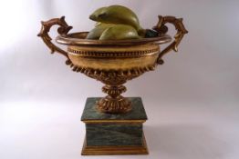 A decorative two handled carved urn on simulated marble base, containing carved and painted fruit,