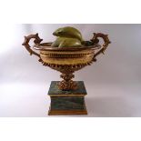 A decorative two handled carved urn on simulated marble base, containing carved and painted fruit,
