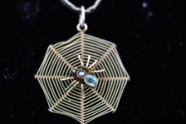 A yellow metal spider web pendant having a central spider set with aquamarine and seed pearl.