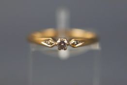 A yellow gold ring set with a single diamond and two smaller diamonds to the shoulders.