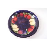 A Moorcroft earthenware shallow dish with plum pattern on a deep blue ground,