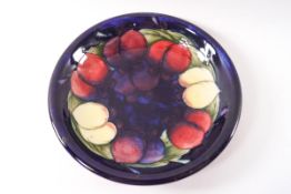 A Moorcroft earthenware shallow dish with plum pattern on a deep blue ground,