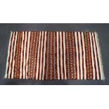 A Moroccan flat weave kelim with red stripes and metal sequins on a neutral ground,