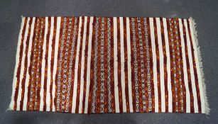 A Moroccan flat weave kelim with red stripes and metal sequins on a neutral ground,