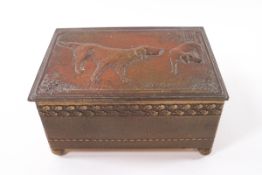 An embossed brass cigarette box, the top decorated with two pointers, on ball feet,