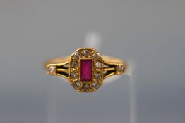 A yellow gold dress ring set with a central rectangular ruby and twelve round brilliant diamonds.