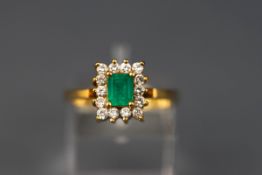 A modern yellow gold cluster ring set with a rectangular emerald and fourteen round brilliant
