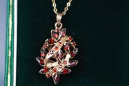 A yellow gold pendant of abstract design set with marquise and round garnets.