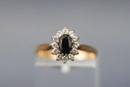 A yellow gold cluster ring set with an oval black sapphire and twelve round cubic zirconias.