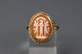 A yellow gold ring set with a shell cameo depicting three females.