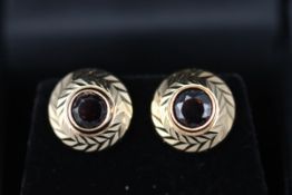 A yellow gold pair of single stone stud earrings each insert with a round garnet.