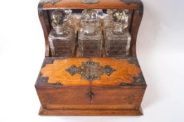 A late Victorian oak three bottle tantalus with plated mounts and compartmental storage interior,