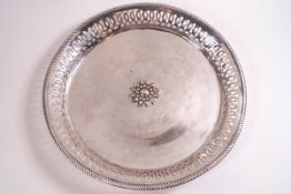 A white metal circular dish with pierced border and central flower motif,