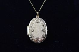 A yellow gold oval locket with floral engraved design suspended from a fine cub link chain.