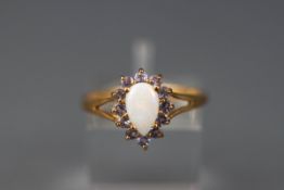 A yellow gold cluster ring set with a pear shape cabochon opal and twelve round cut tanzanites.