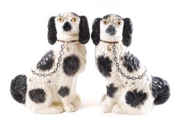 A pair of Staffordshire pottery black and white spaniels with gilt painted chains,