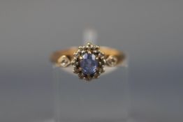 A yellow gold cluster ring set with an oval tanzanite and fourteen single cut diamonds.