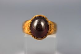 A yellow gold single stone ring set with a cabochon garnet.