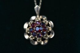 A yellow gold ornate pendant set with nine round garnets.