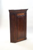 A George III mahogany hanging corner cabinet with dental cornice above a blind fretwork frieze with