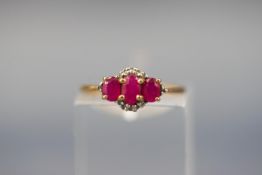 A yellow gold ring set with three oval rubies and twelve variable single cut diamonds.