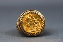 A yellow gold ring set with a 1915 full Sovereign. Scroll engraved shoulders and plain shank.