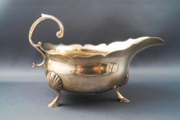 A George II silver sauceboat, with flying scroll handle, shaped rim, on three shell and hoof feet,