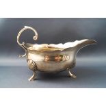 A George II silver sauceboat, with flying scroll handle, shaped rim, on three shell and hoof feet,