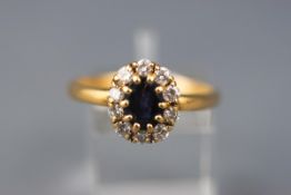 A yellow gold cluster ring set with an oval sapphire and ten round brilliant diamonds.