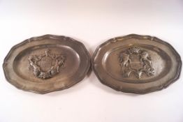 A pair of pewter shaped oval plates, each embossed with a coat of arms,