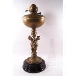 A Victorian brass oil lamp supported by two cast cherubs on black earthenware plinth,