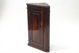 A small 18th century oak corner cupboard with panelled door enclosing two shelves,
