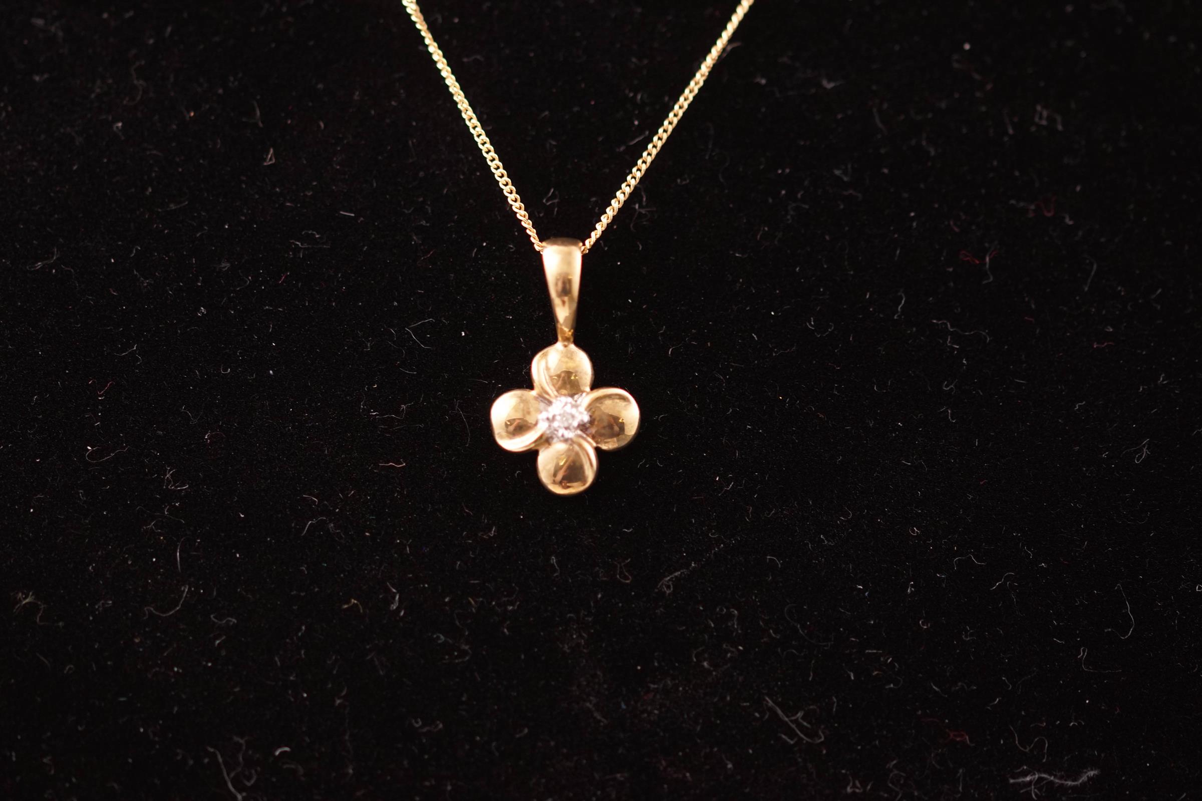 A yellow metal flower pendant set with a 0.01ct single cut diamond.