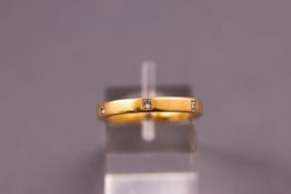A yellow metal band ring set with six princess cut diamonds. Hallmarked 18ct gold. Size L.