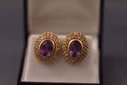 A yellow metal pair of earrings each set with an oval cut amethyst. post and clip fitting.