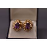 A yellow metal pair of earrings each set with an oval cut amethyst. post and clip fitting.