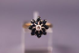 A yellow metal cluster ring set with a central diamond and surrounded by sapphires. Stamped 18ct.