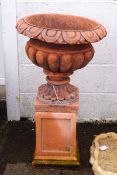 A pair of re-constituted stone garden urns and plinths with terracotta finish,