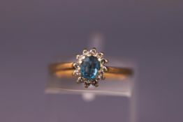 A yellow metal cluster ring set with an oval blue topaz surrounded by diamonds. Hallmarked 9ct gold.