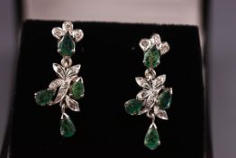A pair of white metal drop earrings set with emeralds and single cut diamonds.